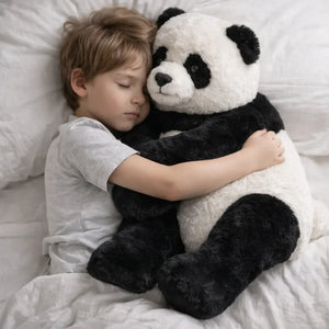 Child hugging a large panda plush toy on a bed